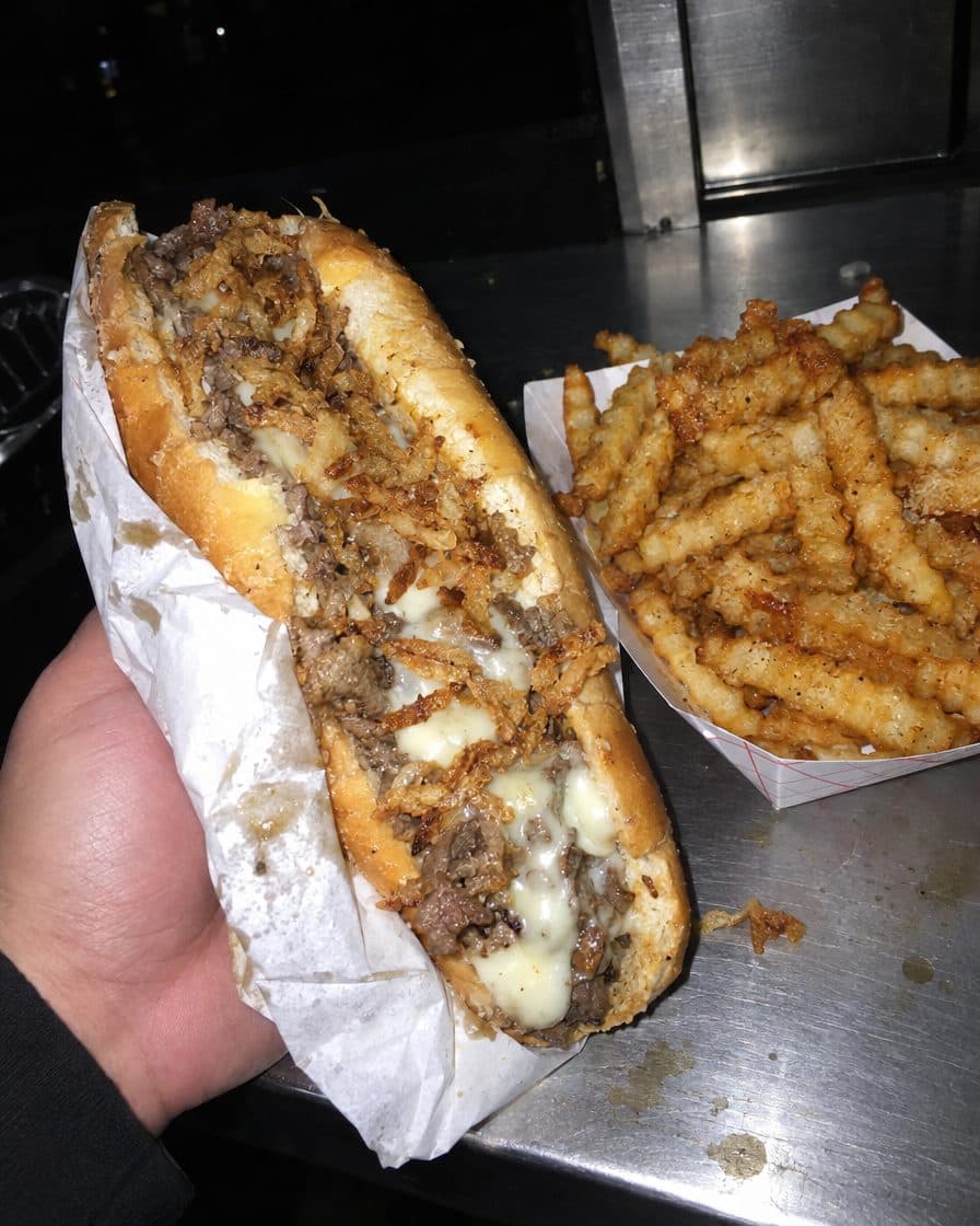 A cheesesteak and crinkle fries on a takeout counter